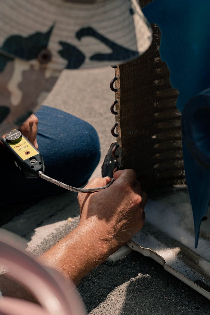 Technician repairing an air conditioner unit with tools, showcasing detailed maintenance process.