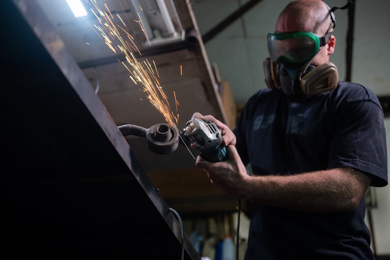 Man wearing safety gear grinding metal indoors with sparks flying.